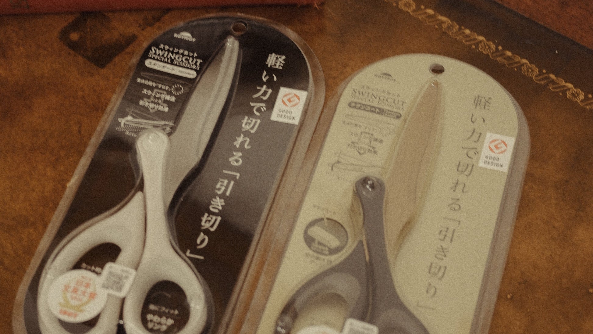 Two pairs of scissors in packaging on a wooden surface
